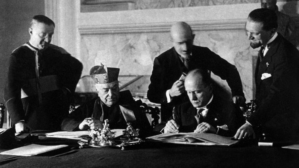 Historical black-and-white image of Mussolini and Vatican officials during the Lateran Treaty signing.

